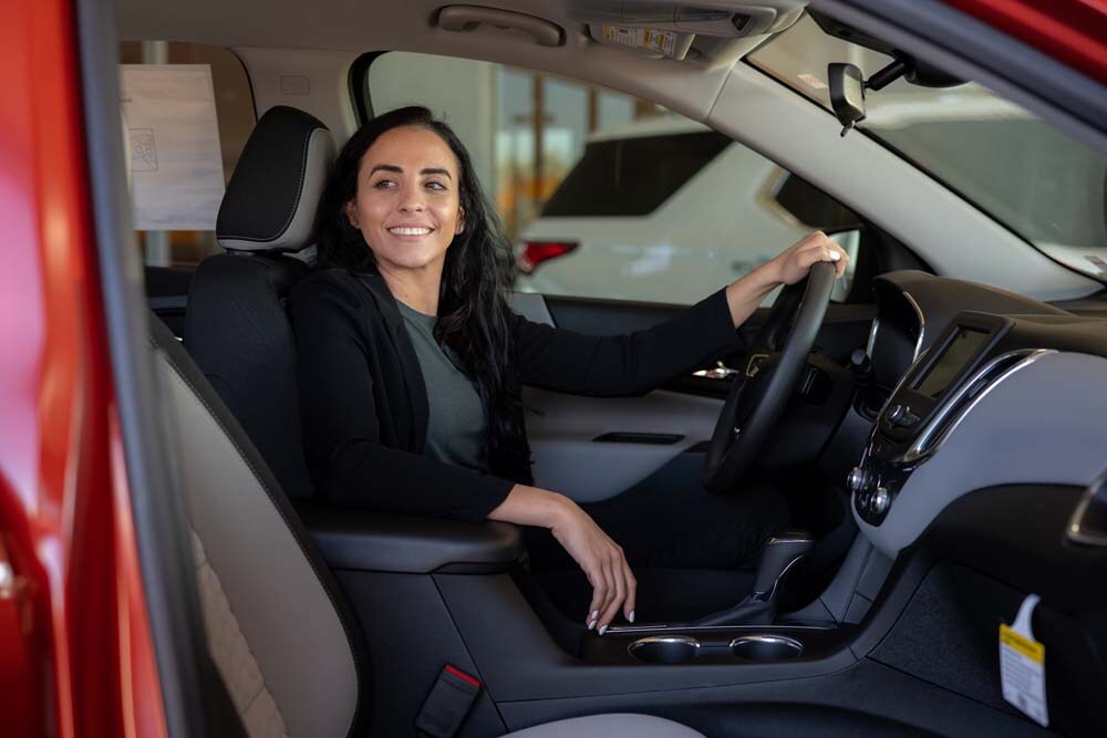 Image of a woman smiling in the driver's seat of a red car